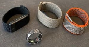 Smart ring and three screenless fitness bands displayed on a wooden table for a side-by-side comparison of the best screenless fitness trackers in 2026.