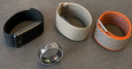 Smart ring and three screenless fitness bands displayed on a wooden table for a side-by-side comparison of the best screenless fitness trackers in 2026.